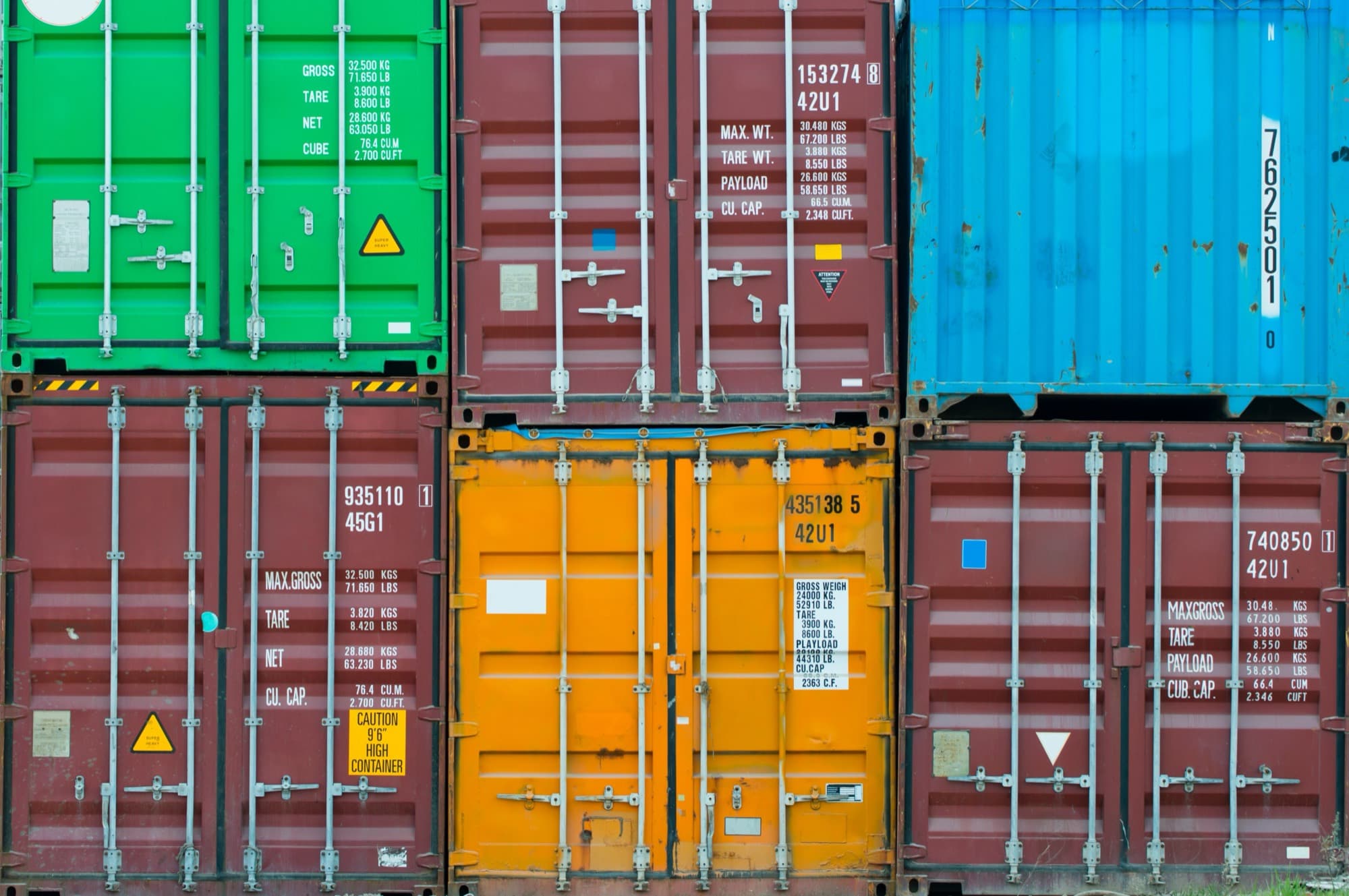 Shipping containers stacked two high in green, maroon, blue and orange, seen from the door end